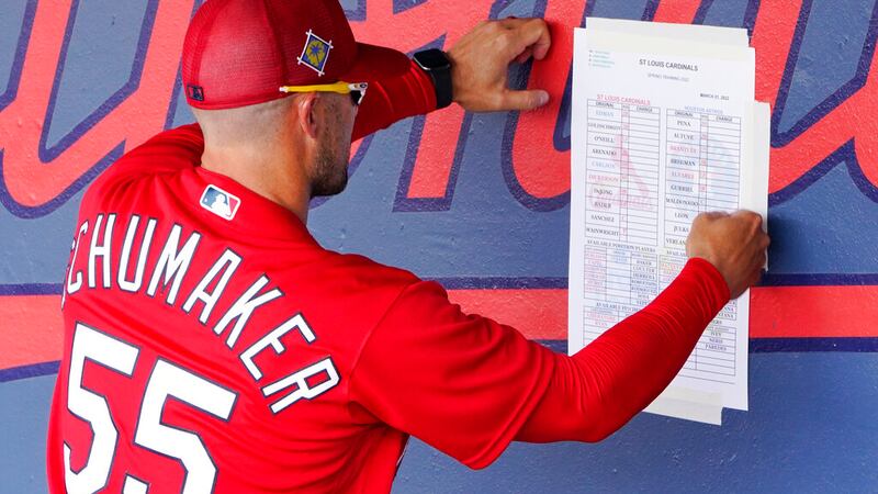 St. Louis Cardinals bench coach Skip Schumaker tapes a line-up to the dugout wall before a...